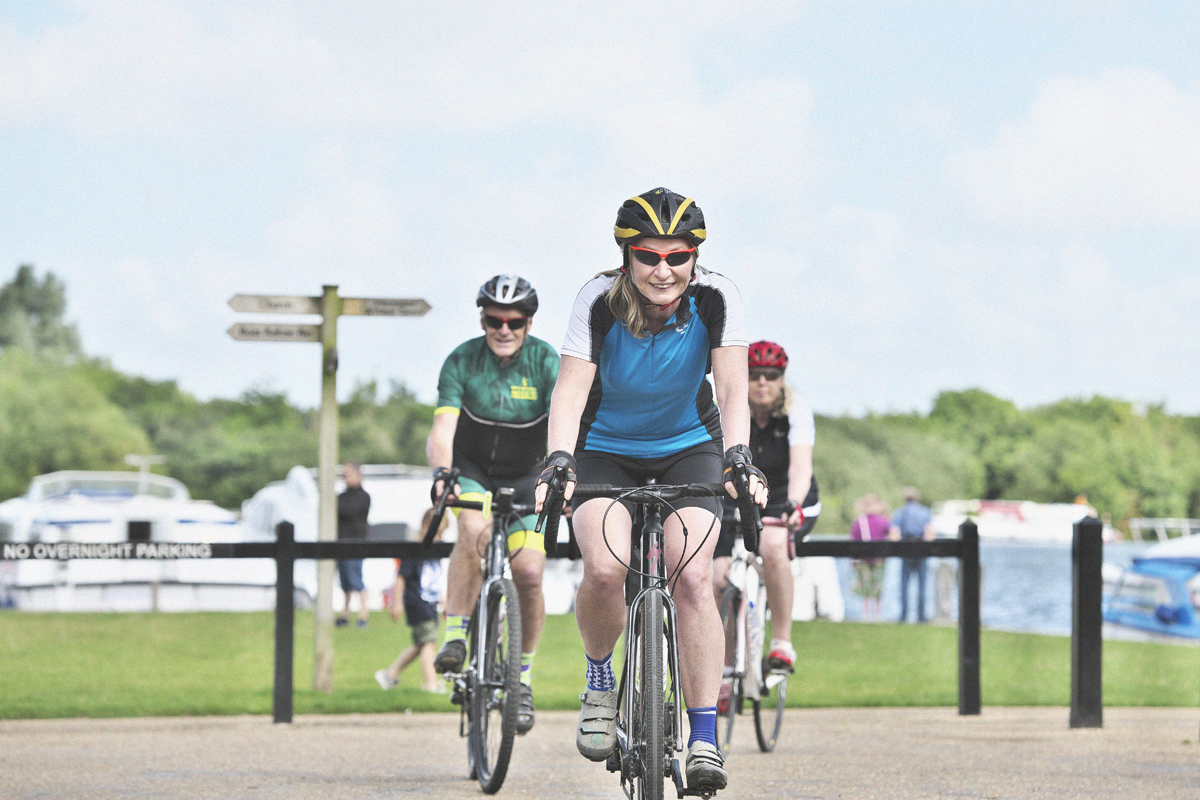 Three cyclists ride near the Broads looking towards the camera