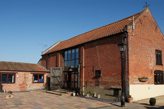 A large red brick barn and paved courtyard area, a sunny day with clear blue skies behind the barn