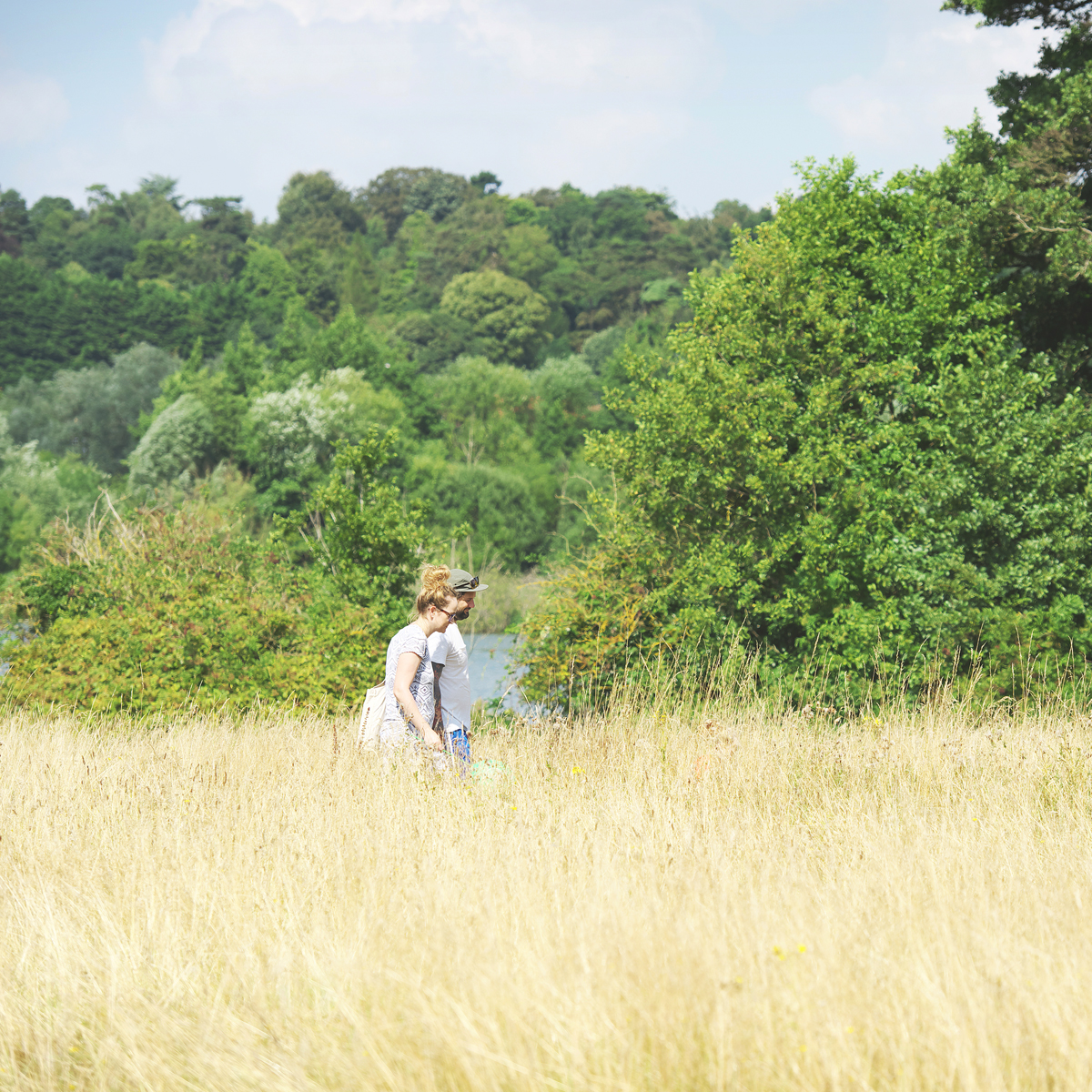 Two people walking infront of the grassy, leafy surroundings of Whitlingham Country Park
