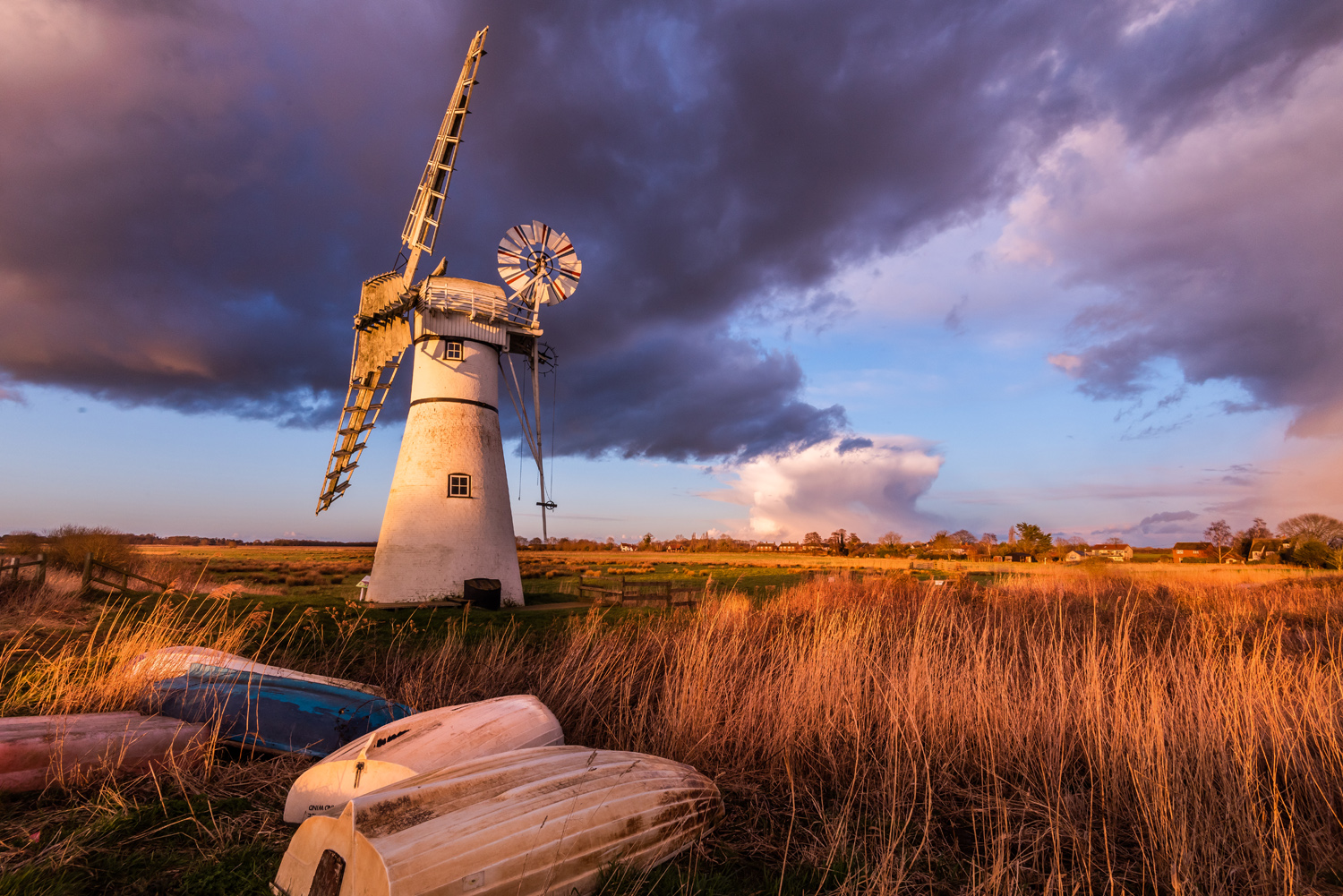 Thurne Mill during a stormy golden hour, with golden reeds and an upturned boat in the foreground, by Visit the Broads 