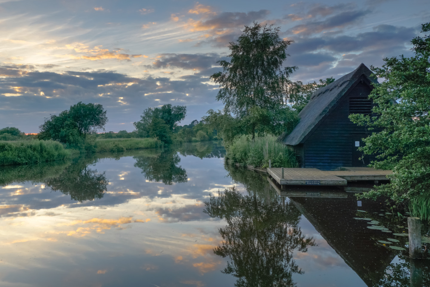 Reflections of the sky and thatched boatshed in the still water of the River Ant, by Chris Hill