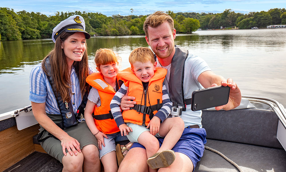 A family of 4 taking a selfie on a day boat in the Norfolk Broads, The 2 children wearing bright orange bouyancy aids.