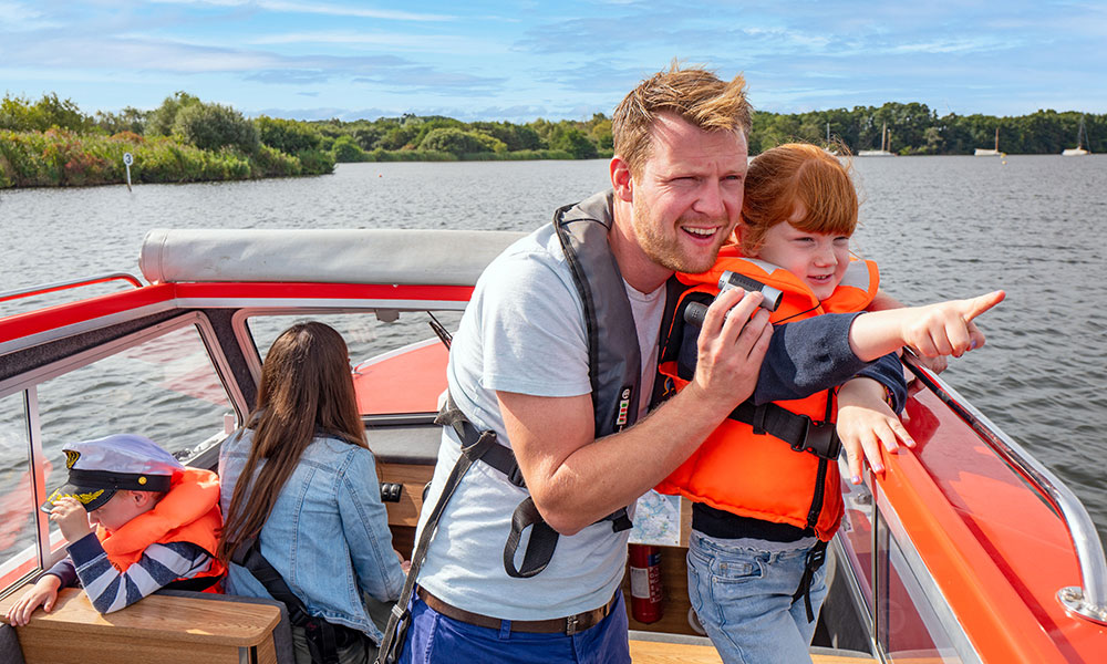 Three people enjoying the view from a dayboat on the Norfolk Broads