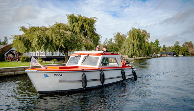 A Richardson's dayboat on the Norfolk Broads, with trees on the riverside behind
