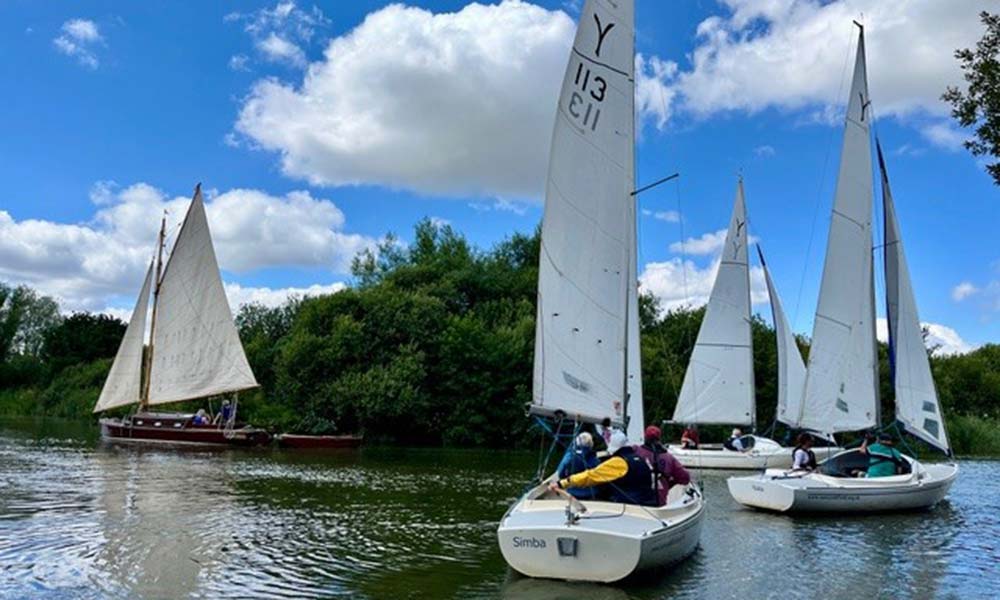 6 accessible sailing boats, with their sails up, and a stunning blue sky