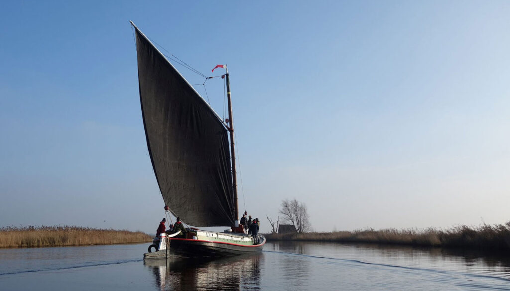 Wherry Maud sailing on a very peaceful river. With black sail catching the breeze.
