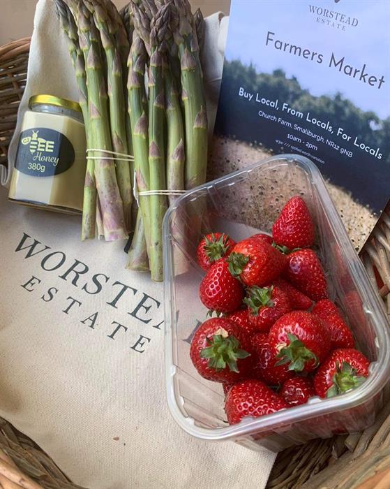 A punnet of ripe strawberries and a bunch of fresh asparagus sat on an Worstead Estate branded bag