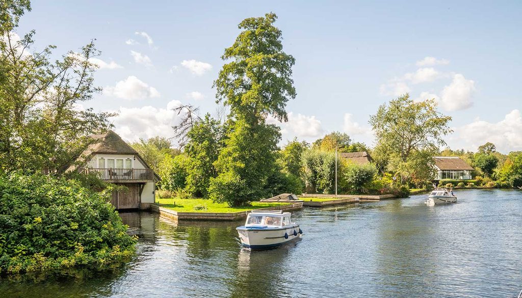 A Broads dayboat on the river, with thatched cottages on the banks